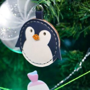 Выкройка кожаного брелока или игрушки в виде пингвина для новогодней ёлки на белом фоне.